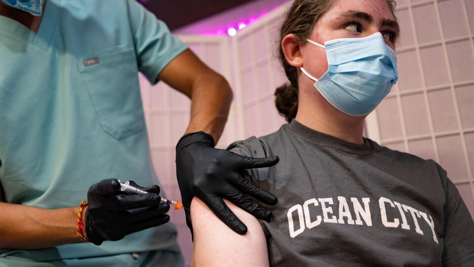 Un adolescent de 14 ans portant un t-shirt sur lequel sont écrits les mots « Ocean City » regarde devant lui pendant qu'un infirmier en vêtements d'hôpital le vaccine dans le bras droit.