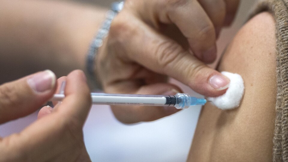 Une personne injecte une dose de vaccin dans un bras. 