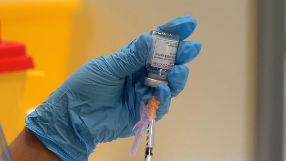 Un gros plan d'une main tenant une seringue et une dose de vaccin contre la COVID-19. 