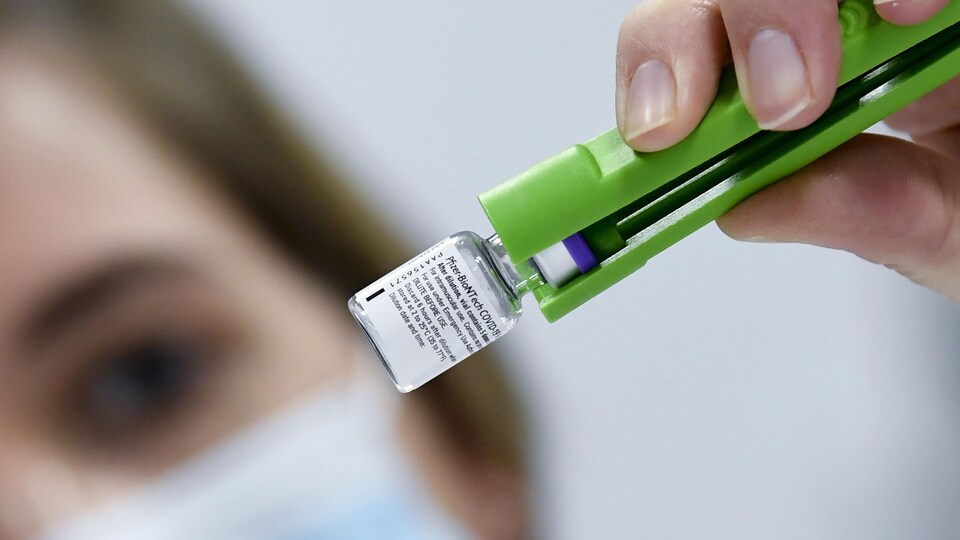 Une technicienne de laboratoire manipule avec des pinces une fiole de vaccin qui doit décongeler.