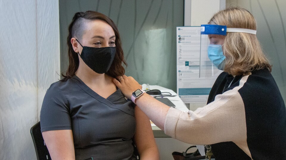 Danielle Sheaves assise sur une chaise. Elle reçoit une dose du vaccin.