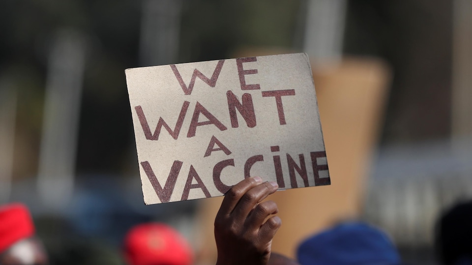 Un manifestant tient une affiche sur laquelle est écrit «We want a vaccine» («Nous voulons un vaccin»).