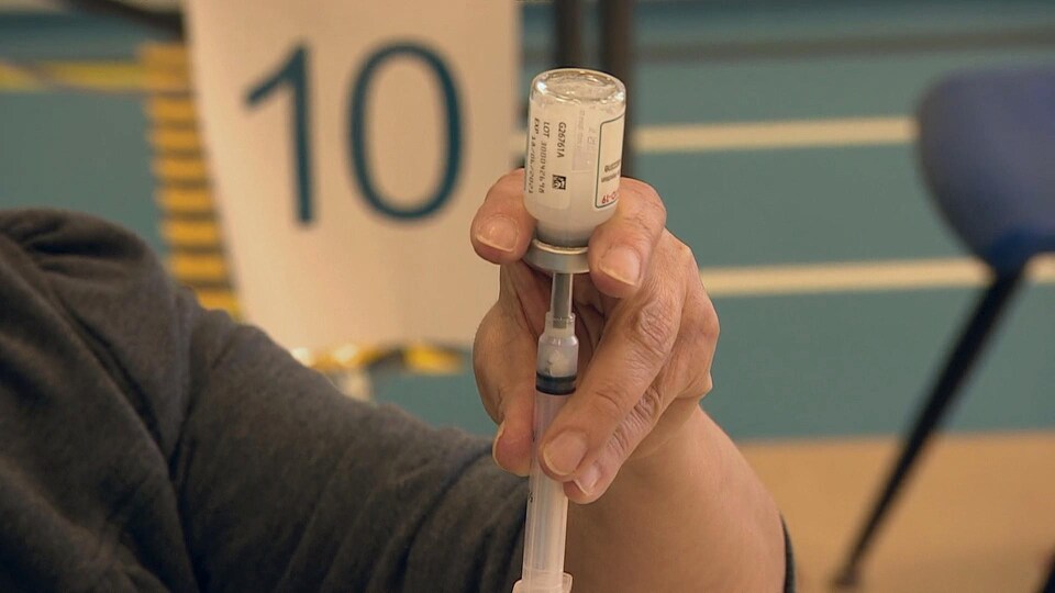 Gros plan sur la main d'une personne qui tient une fiole du vaccin et aspire une dose dans une seringue.