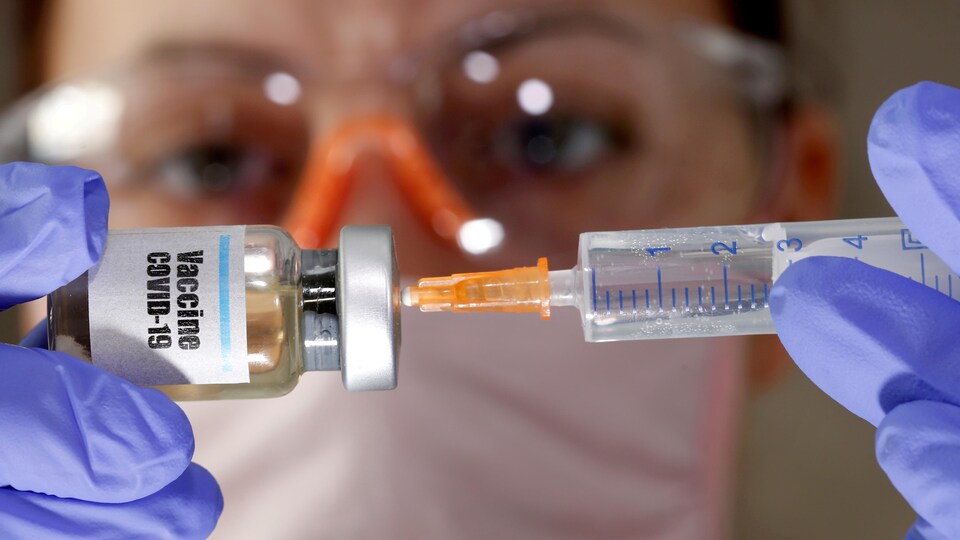 Une femme tient un petit flacon portant un autocollant «Vaccin COVID-19» et une seringue médicale.