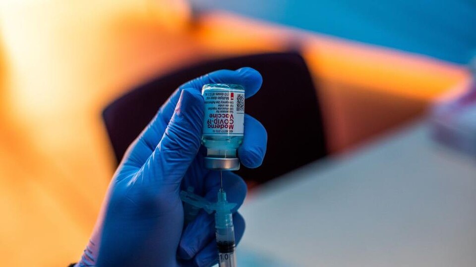 Un membre du personnel médical extrait une dose du vaccin Moderna d'une fiole à l'aide d'une seringue.