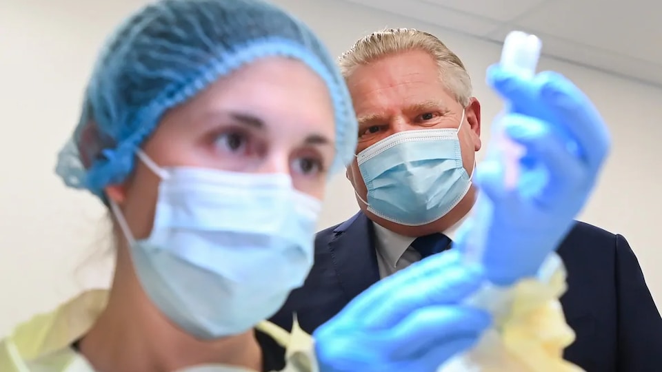 Le premier ministre de l'Ontario, Doug Ford, observe une infirmière préparer une dose du vaccin contre la COVID-19.