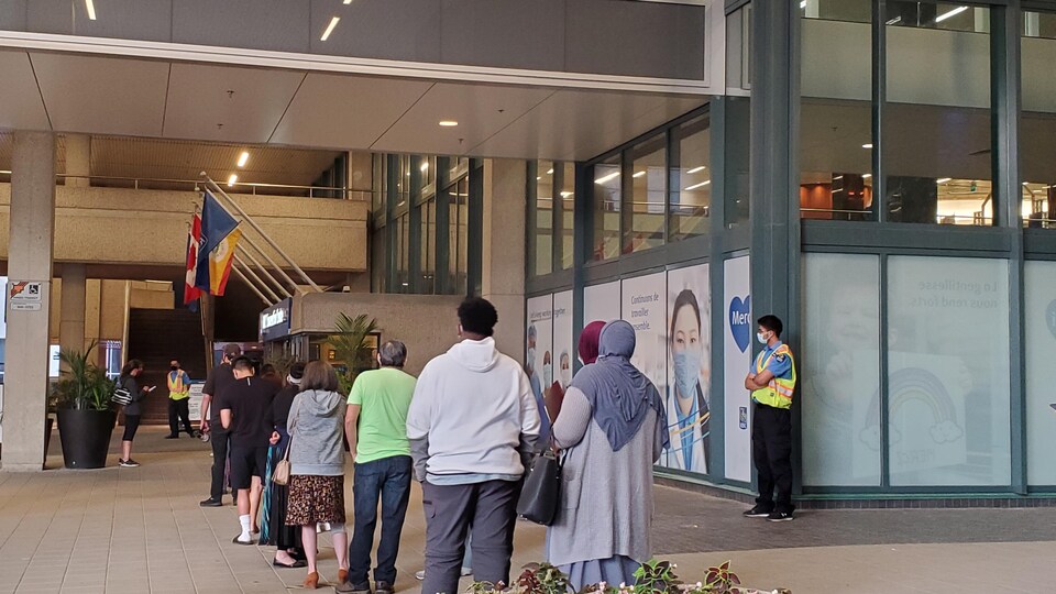 Une dizaine de personnes font la file à l'extérieur pour rentrer dans le RBC Convention Centre de Winnipeg pour recevoir une dose de vaccin, sous l'oeil d'agents de sécurité.