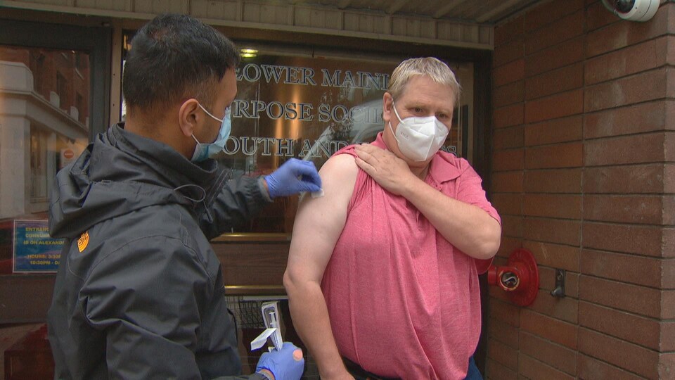 Un homme se prépare à recevoir un vaccin à l'extérieur d'un établissement.