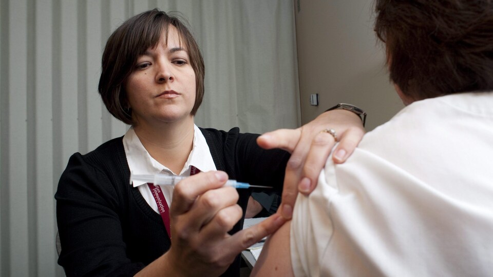 Une infirmière s'apprête à vacciner quelqu'un, qui est de dos.