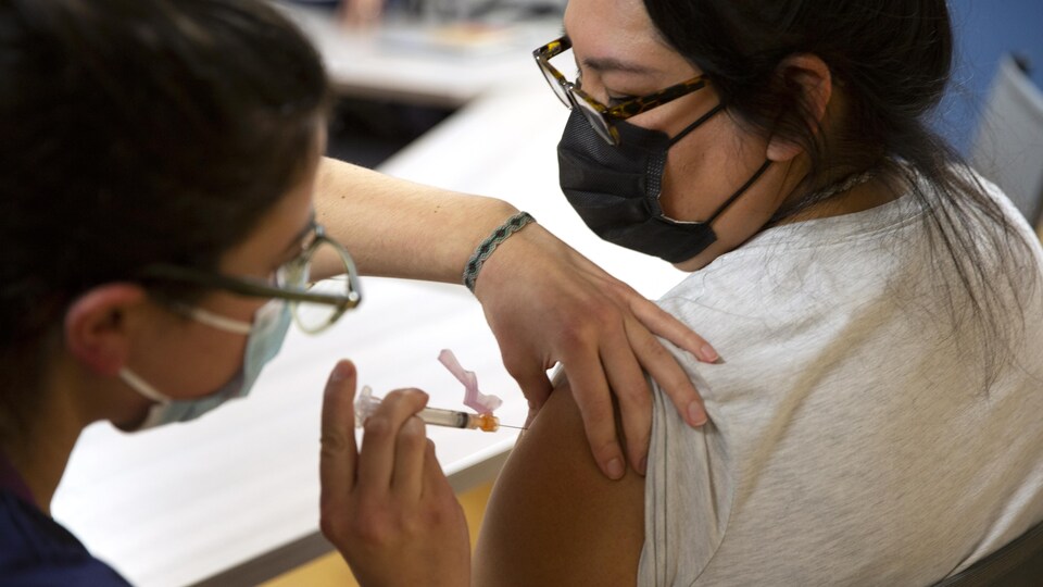 Une femme portant un masque se fait vacciner dans le bras par une infirmière.
