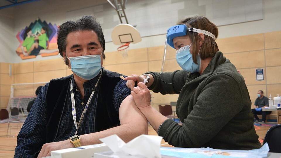 Un homme qui porte un masque se fait inoculer une dose de vaccin par une femme qui porte un masque et une visière de protection.