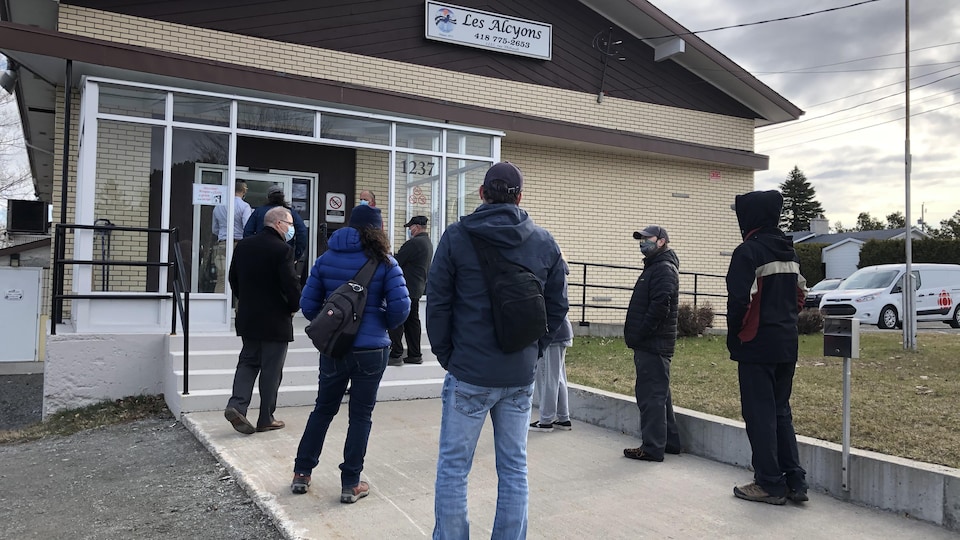 Une dizaine de personnes attendent à l'extérieur d'un bâtiment à Mont-Joli pour se faire vacciner contre la COVID-19.