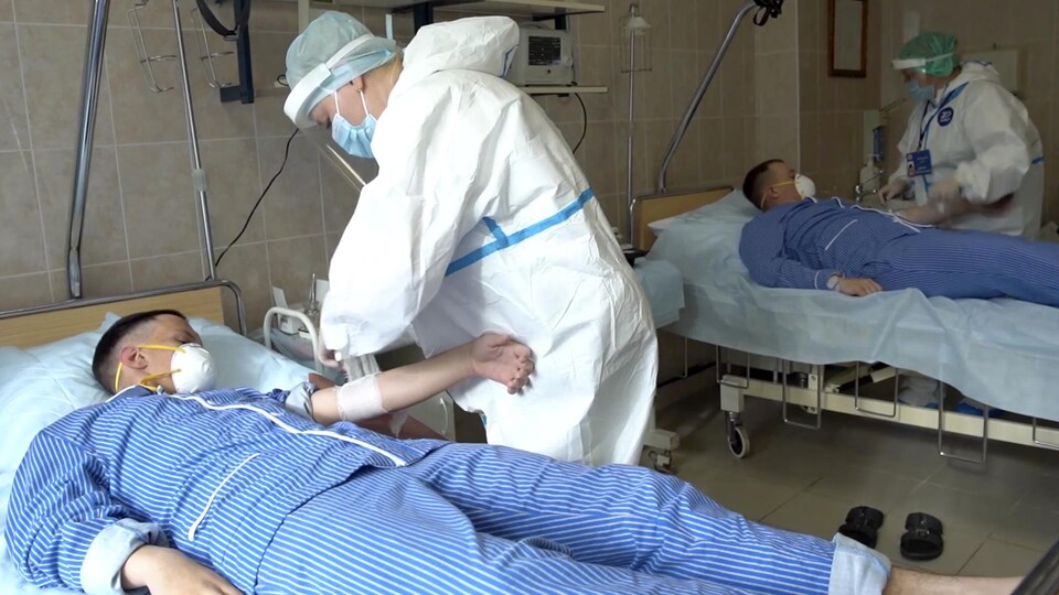 Des spécialistes de la santé vêtus d'uniformes, de masques et de gants s'occupent de patients couchés sur un lit, le visage couvert d'un masque.