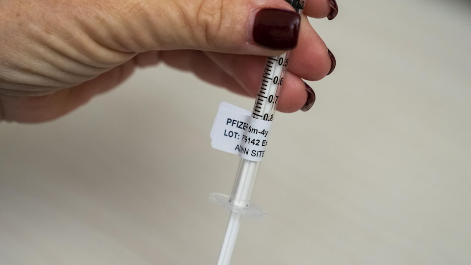 A hand holds a syringe containing a Pfizer vaccine.