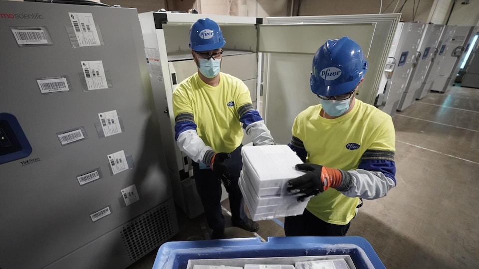Deux employés de Pfizer tiennent des boîtes contenant le vaccin Pfizer-BioNTech contre la COVID-19.
