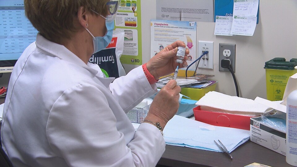 Une infirmière prépare un vaccin dans un bureau.