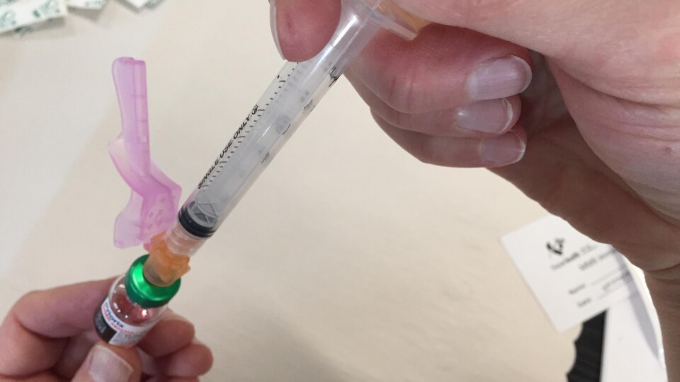 Une main tient une seringue contenant le vaccin.