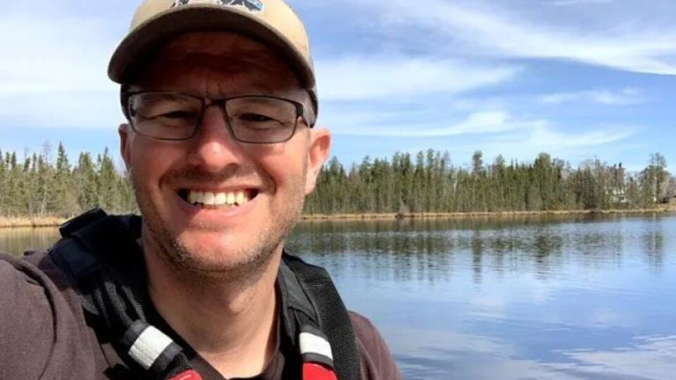 Le pasteur Kyle Penner sourit, avec derrière lui un plan d'eau et des arbres.
