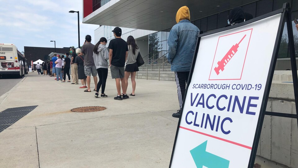Des jeunes font la file à l'extérieur d'un centre de vaccination.