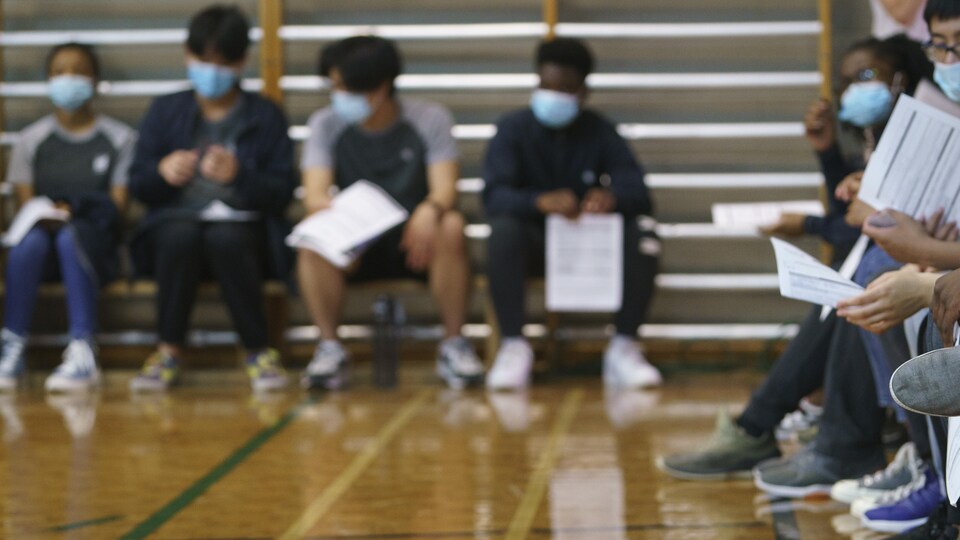 Des jeunes assis dans un gymnase et tiennent leur formulaire de vaccination.