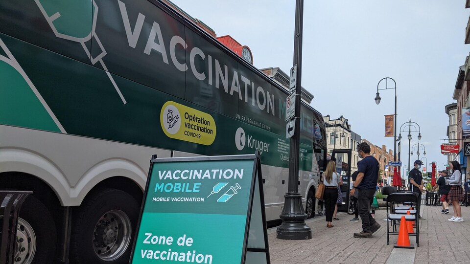 Des gens font la file devant l'autocar qui fait office de clinique mobile de vaccination.
