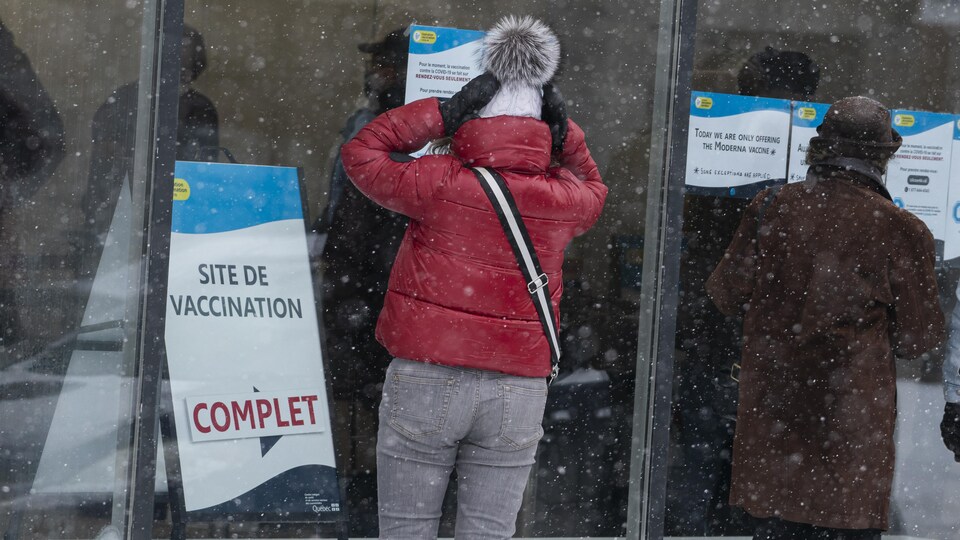 Une femme observe une affiche « complet » devant une clinique de vaccination.