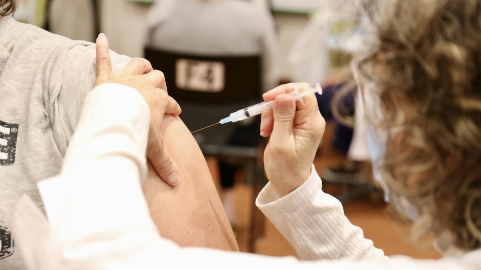 Une vaccinatrice vaccine une personne.