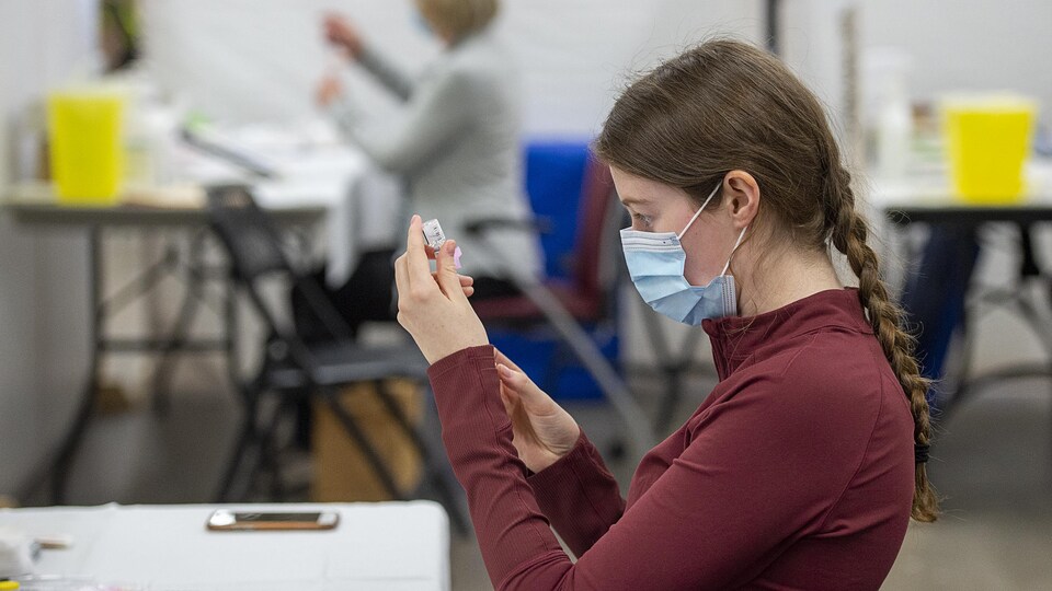 Une femme de profil qui prépare une dose de vaccin.