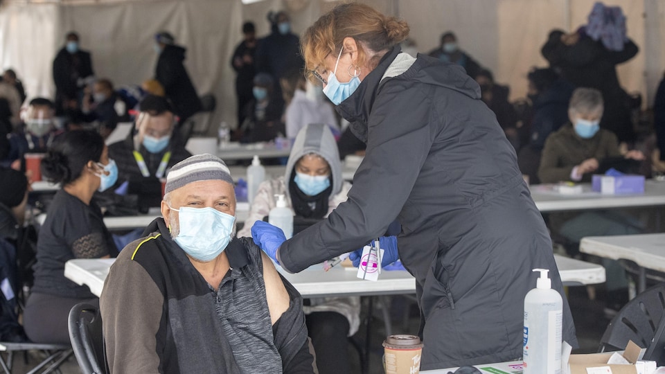 Une infirmière vaccine un homme sous une grande tente.