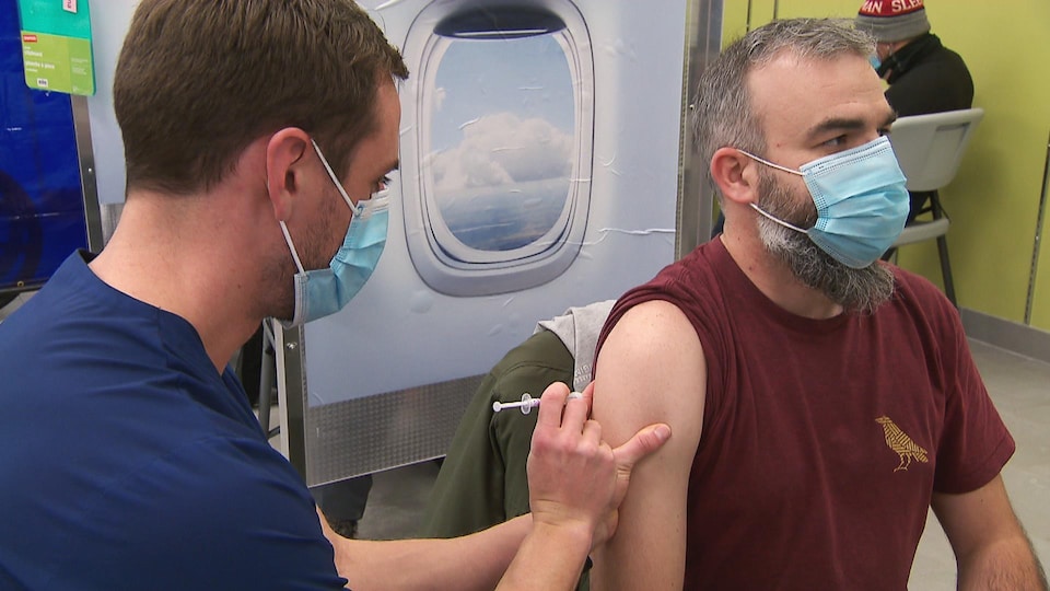 Un travailleur de la santé s’apprête à injecter une dose de vaccin contre la COVID-19 dans le bras droit d’un homme.