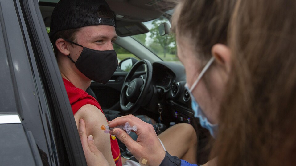 Une personne dans une voiture reçoit une dose de vaccin contre la COVID-19.