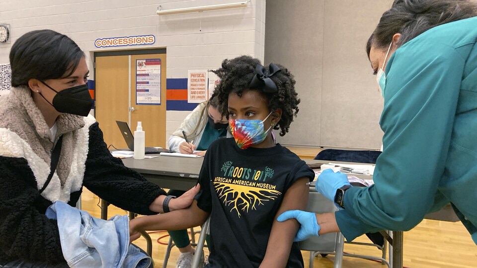 Cadell Walker tient la main de sa file Solome, 9 ans, qui se fait vacciner contre la COVID-19.