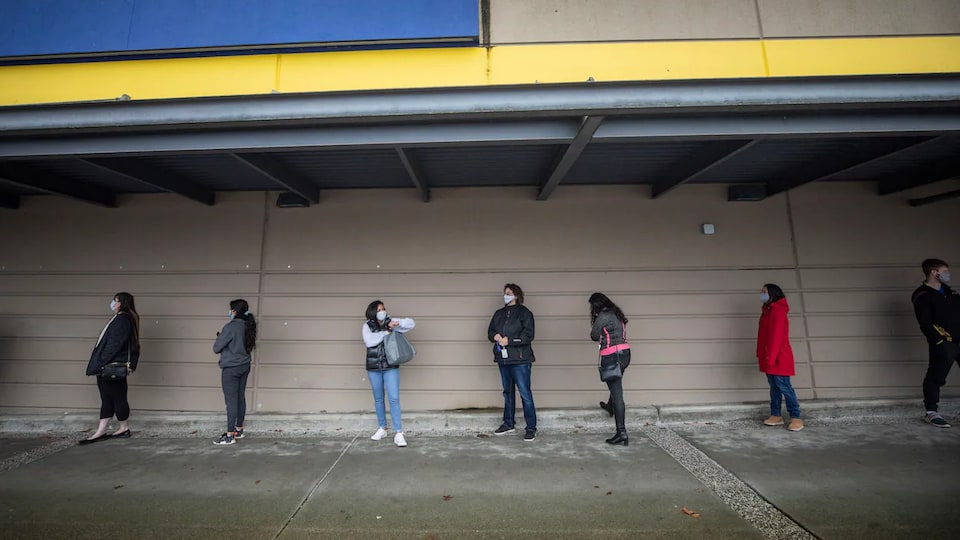 Le personnel d'écoles et des enseignants du district scolaire de Surrey portants un masque font la queue à l'extérieur pour se faire vacciner contre la COVID-19.