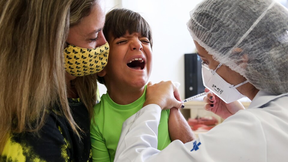 Le jeune Brésilien Leonardo Larussi crie dans les bras de sa mère en recevant une dose du vaccin de Pfizer.