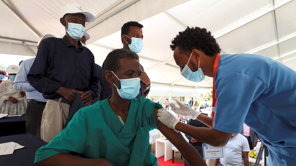Des gens attendent derrière l'homme en train de se faire vacciner.