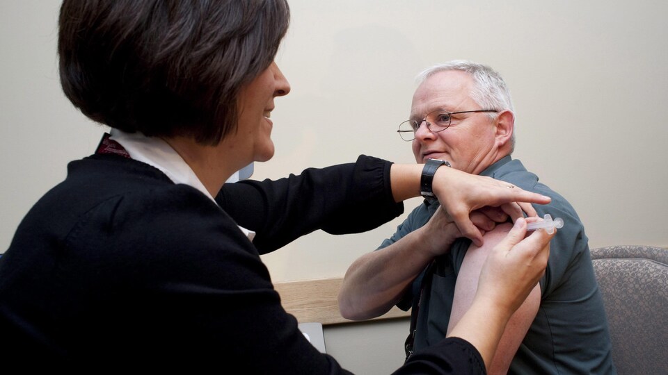 Un homme est assis et reçoit dans son bras gauche le vaccin administré par l'infirmière.