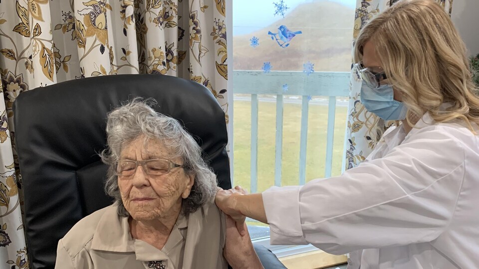 Une personnes âgée reçoit un vaccin, les yeux fermés.