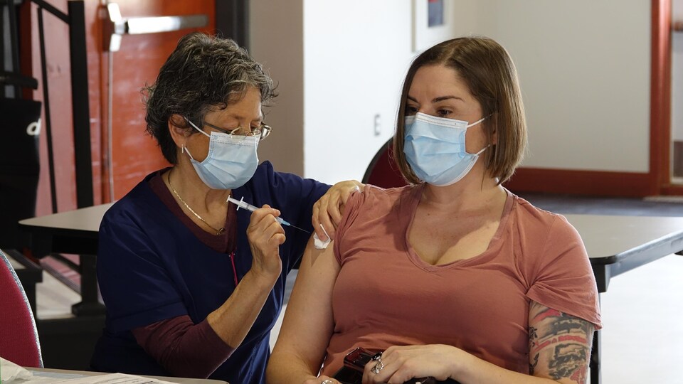 Une femme masquée reçoit le vaccin d'une autre dame masquée.