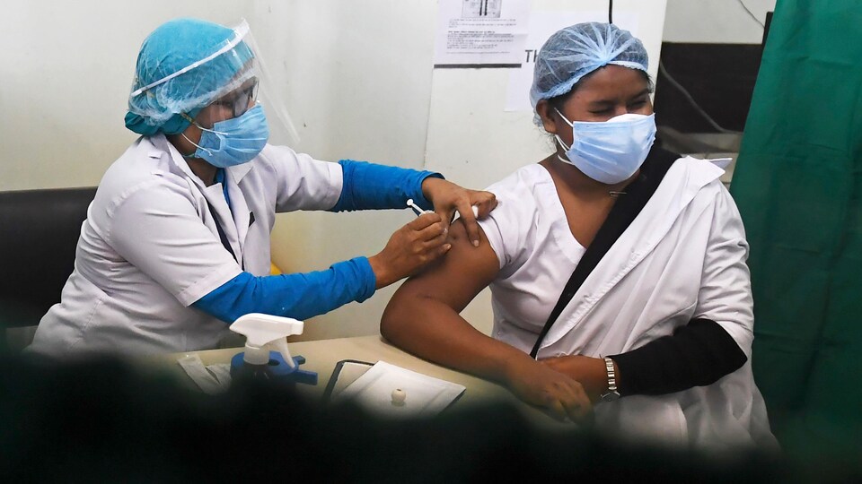 Une femme masquée se fait vacciner par un médecin qui porte lui aussi un masque ainsi qu'une visière.