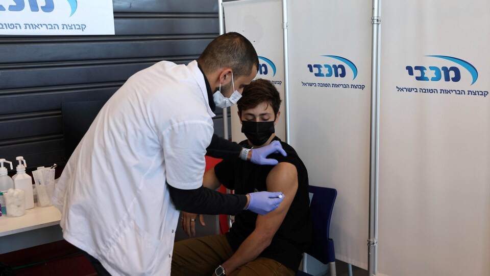 Un infirmier administre un vaccin à un adolescent assis sur une chaise.
