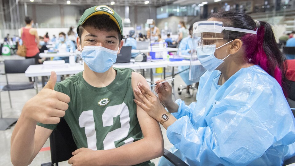 Le jeune homme lève le pouce pendant qu'il se fait vacciner.