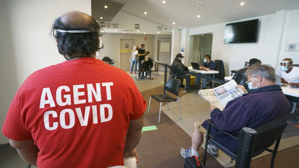 Un homme de dos avec un t-shirt sur lequel on peut lire : «Agent COVID».