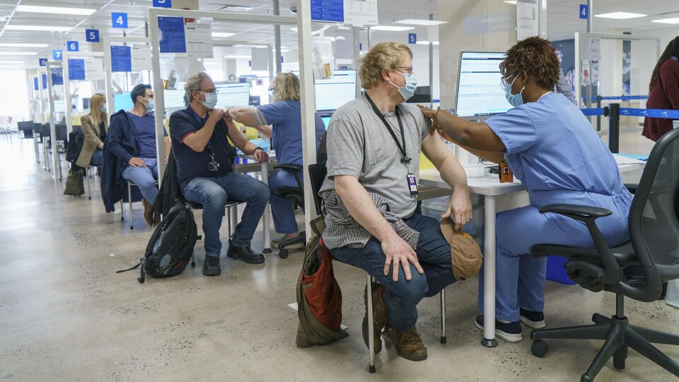 Quatre personnes se font vacciner dans différents cubicules.