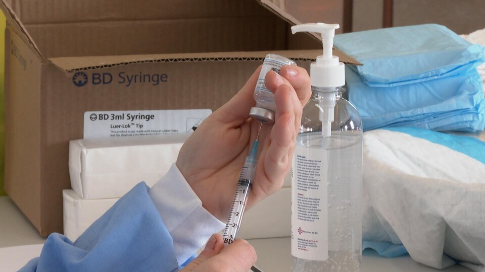 Une infirmière calcule la quantité de vaccin à l'aide d'une seringue. L'aiguille est plantée dans une fiole.