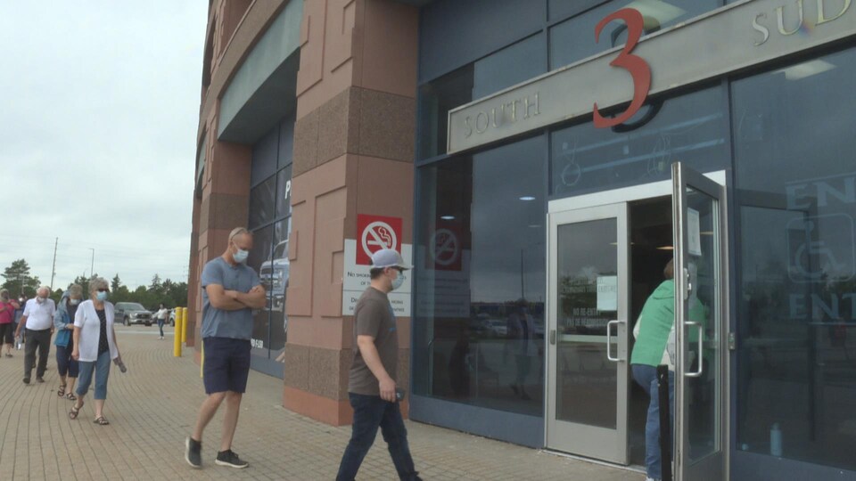 Des gens portant un masque entrent au Centre Canadian Tire pour se faire vacciner.