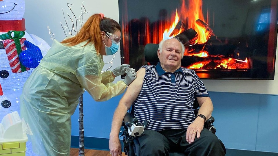 Une infirmière vaccine un homme assis dans un fauteuil roulant électrique.