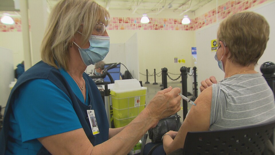 Une infirmière vaccine une personne que l'on voit de dos dans le bras gauche.