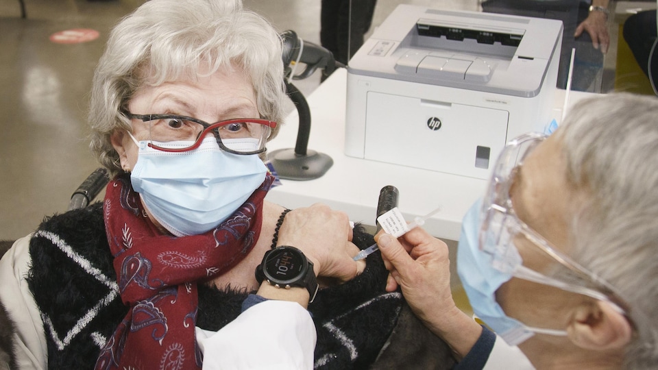 Une femme masquée lève les sourcils en se faisant vacciner.
