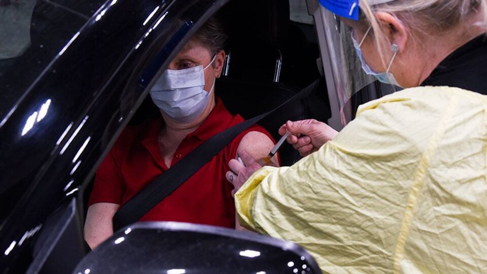 Une infirmière injecte une dose de vaccin à une personne assise dans sa voiture.