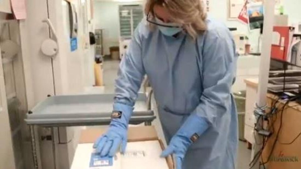 Une travailleuse de la santé ouvre la boîte contenant des doses du vaccin Pfizer-BioNTech à l’Hôpital régional de Miramichi.